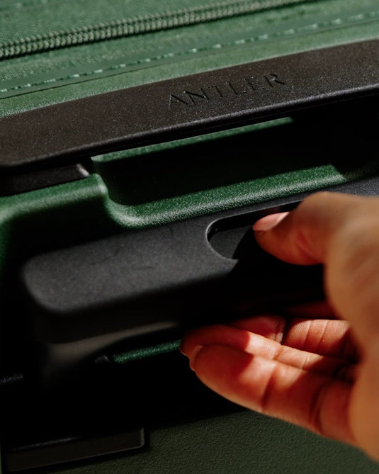 a hand holding a handle of a green suitcase