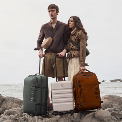 a man and woman standing on rocks with luggage