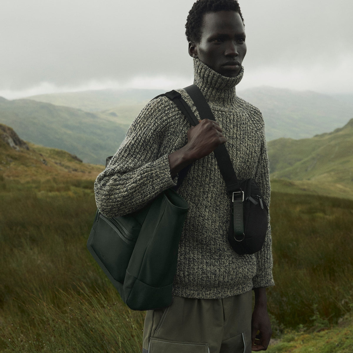 a man standing in a grassy area with a bag on his shoulder