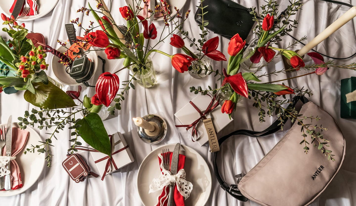 a table with red flowers and a plate and a purse