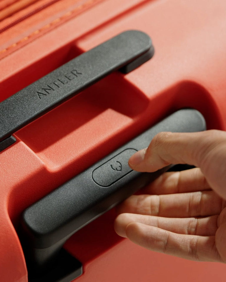 a hand pressing a button on a red suitcase