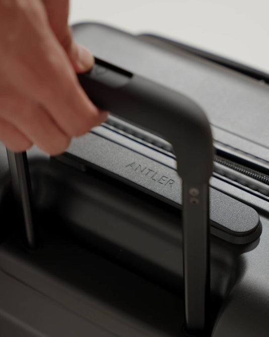a hand holding a handle on a black suitcase
