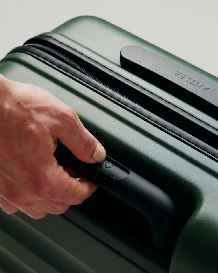 a hand holding a handle on a green suitcase