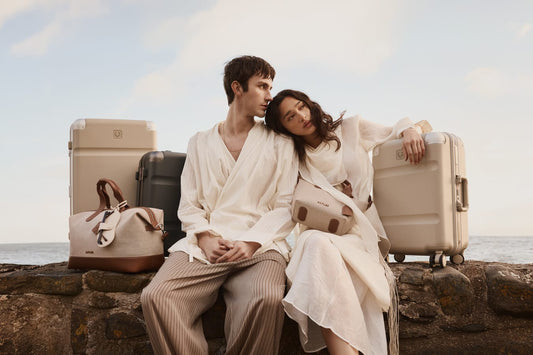 a man and woman sitting on a rock ledge with luggage