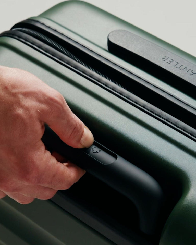 a hand holding a handle on a green suitcase