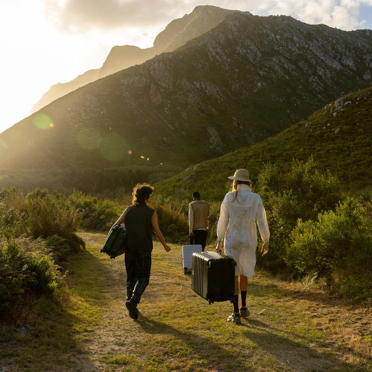 a group of people walking with luggage on a path in the mountains