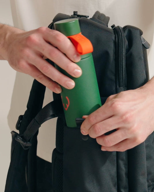 a person holding a green bottle in a black backpack